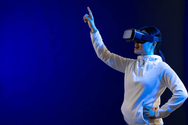 Happy asian woman using vr headset in studio with blue light with copy space. Virtual reality and digital interface technology. - Photo, image