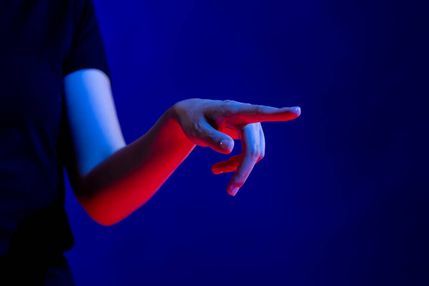 Exposed hand pointing finger in studio with blue light with copy space. Virtual reality and digital interface technology. - 写真・画像