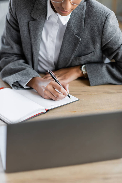 cropped view of african american businesswoman in grey blazer writing in blank notebook on desk in office - Φωτογραφία, εικόνα