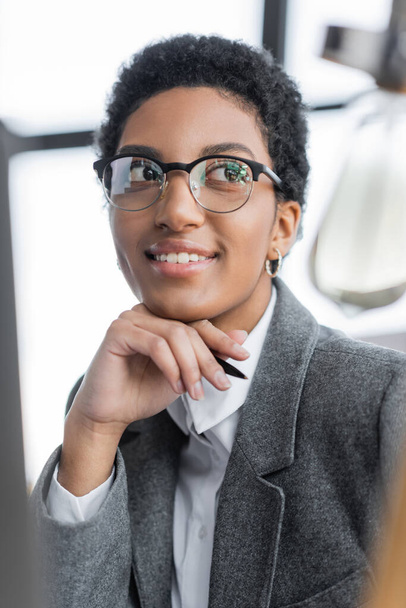 Porträt einer glücklichen und erfolgreichen afrikanisch-amerikanischen Geschäftsfrau mit stylischer Brille, die im Büro wegschaut - Foto, Bild