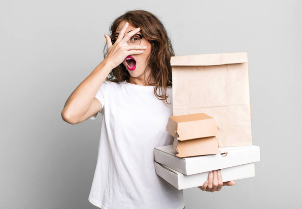 hispanic pretty woman looking shocked, scared or terrified, covering face with hand. take away fast food packages concept - 写真・画像