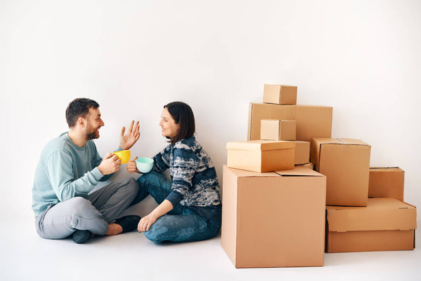 幸せな気楽なカップルの床の上に新しいアパートで移動中の日に座って話している。不動産、関係、家族の概念 - 写真・画像