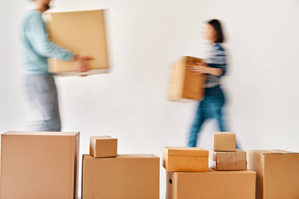 Blurred motion of young couple carrying cardboard boxes moving to new house on white background. Relocation concept - Photo, Image