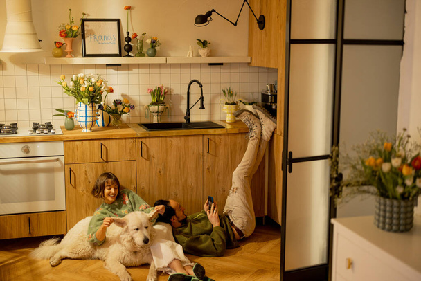 Jong stel zitten ontspannen samen met een schattige hond op keuken thuis. Thuis gezelligheid en huiselijke levensstijl concept - Foto, afbeelding