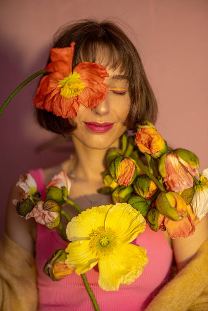 Portrait of a young woman with island poppy cutted flowers on pink background. Concept of beauty and summer - Photo, Image