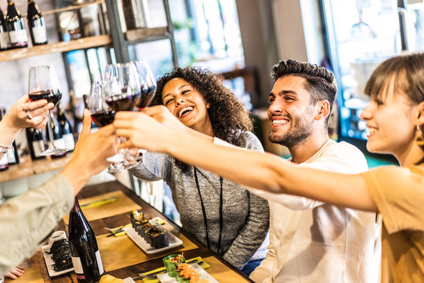 Wieloetniczni przyjaciele wznoszący toast za czerwone wino w restauracji sushi - koncepcja stylu życia żywności i napojów ze szczęśliwymi ludźmi bawiącymi się razem w barze fusion - Ciepły jasny filtr z naciskiem na człowieka w prawo - Zdjęcie, obraz