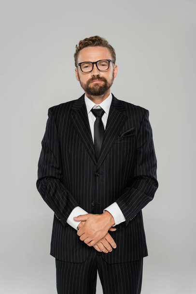 confident and bearded businessman in formal wear and glasses looking at camera isolated on grey  - Photo, image