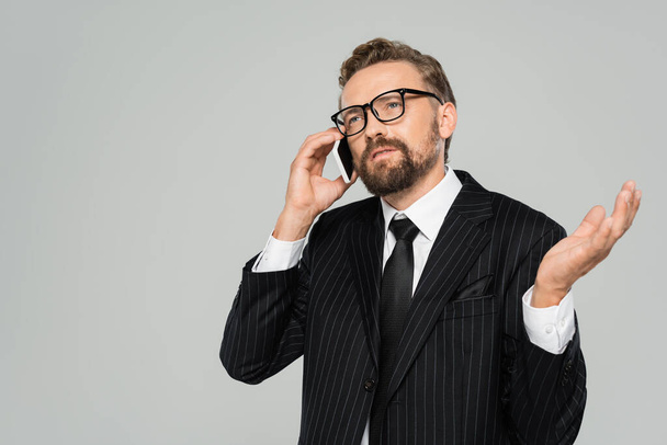 bearded businessman in suit and glasses talking on smartphone isolated on grey  - Fotografie, Obrázek