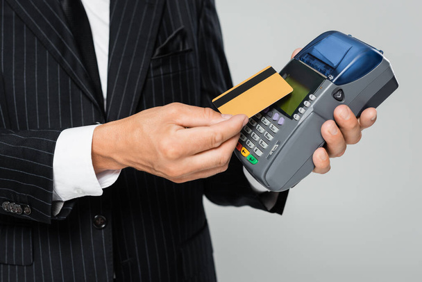 cropped view of businessman in suit holding credit card near payment terminal isolated on grey - Фото, зображення