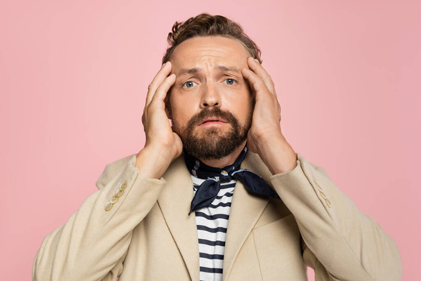 stressed man in blazer and neck scarf looking at camera while holding head isolated on pink - Photo, Image