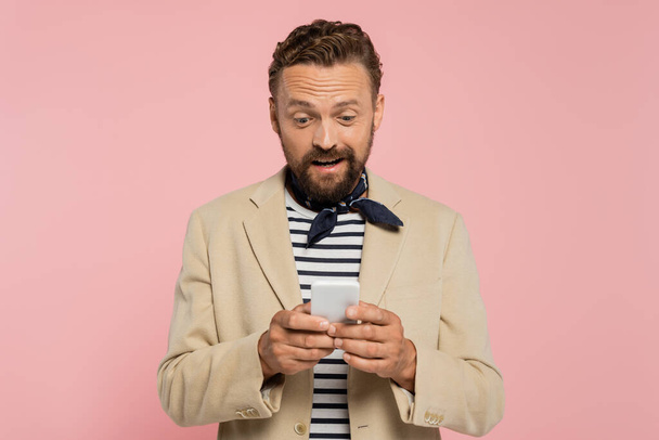 aufgeregter französischer Mann in Blazer und Halstuch-Nachricht auf Smartphone isoliert auf rosa  - Foto, Bild