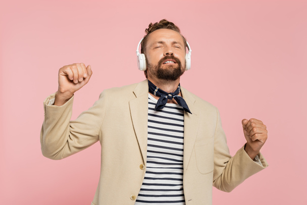 french man in blazer and neck scarf listening music in wireless headphones isolated on pink  - Zdjęcie, obraz