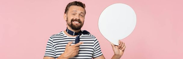 Çizgili tişört ve boyun atkısı giyen mutlu Fransız adam pembe pankartta izole edilmiş konuşma balonu tutuyor.  - Fotoğraf, Görsel