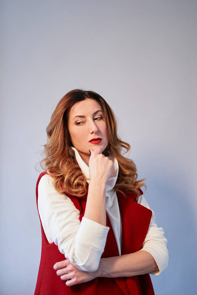 Thinking or dreaming concept. Portrait of a stylish caucasian brunette business lady with wavy hair and brown eyes in elegant maroon suit with crossed arms. Copy space. High quality vertical photo - 写真・画像