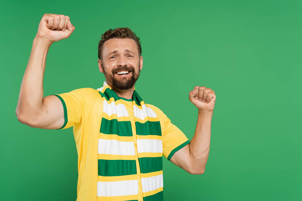 izgatott sport rajongó csíkos sál és sárga póló nézi kamera elszigetelt zöld  - Fotó, kép