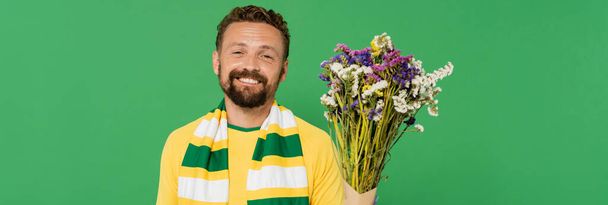 fan de football joyeux et barbu tenant des fleurs sauvages isolées sur vert, bannière  - Photo, image