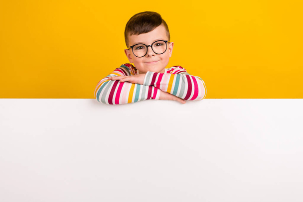 Photo of positive cute boy wear trendy clothes stand behind wall showing empty space isolated on yellow color background. - Foto, afbeelding