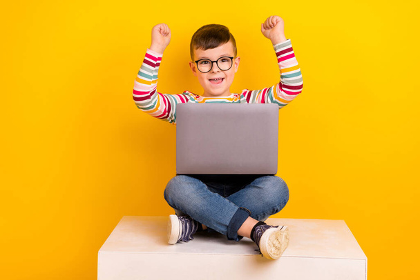 Photo of overjoyed cheerful boy wear stylish clothes sit platform celebrate success passed test exam isolated on yellow color background. - Фото, изображение