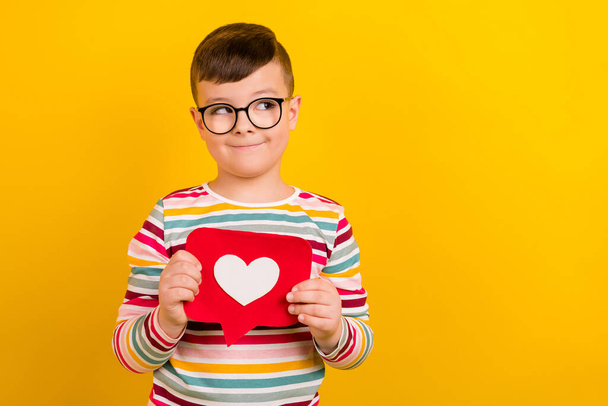 Photo of charming positive pupil boy wear stylish striped clothes hold red paper card look empty space isolated on yellow color background. - Foto, Imagem