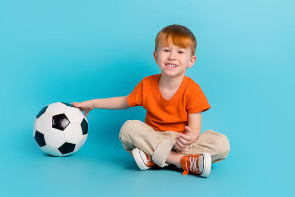 Photo of charming positive cute boy sitting floor enjoy hobby like football watching final league isolated on cyan color background. - Foto, afbeelding