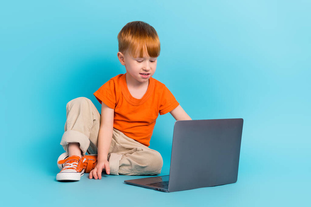 Photo of charming cute little boy sitting floor watching film cartoon online academic classes course isolated on cyan color background. - Valokuva, kuva