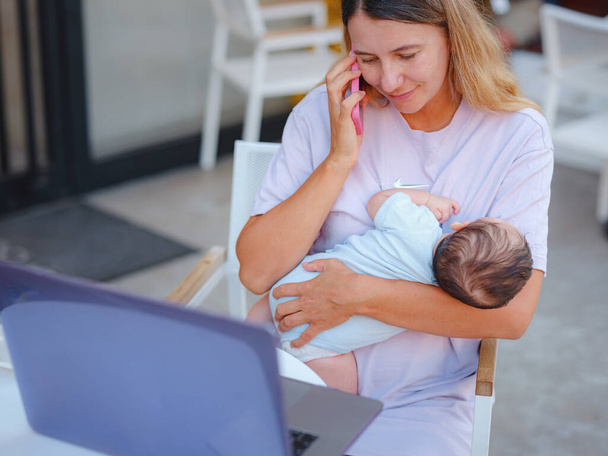 Diverse people portrait. Creative businesswoman balancing work and motherhood. Beautiful young mother working with laptop computer and breastfeeding, holding and nursing her newborn baby at cafe. - Foto, imagen