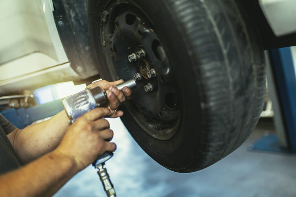 Mechanician changing car wheel in auto repair shop, close up. - Photo, Image