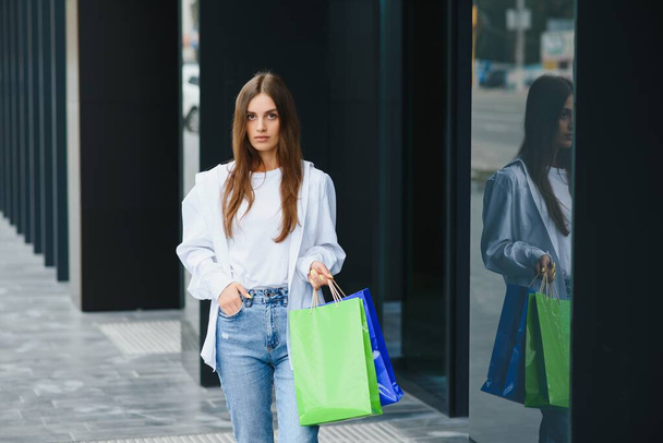 Beautiful young woman with shopping bags near shop outdoors - Foto, afbeelding