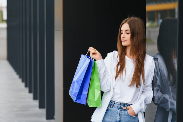 Beautiful young woman with shopping bags near shop outdoors - Photo, Image
