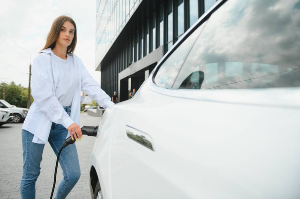 Woman near electric car. Vehicle charged at the charging station - Foto, Bild