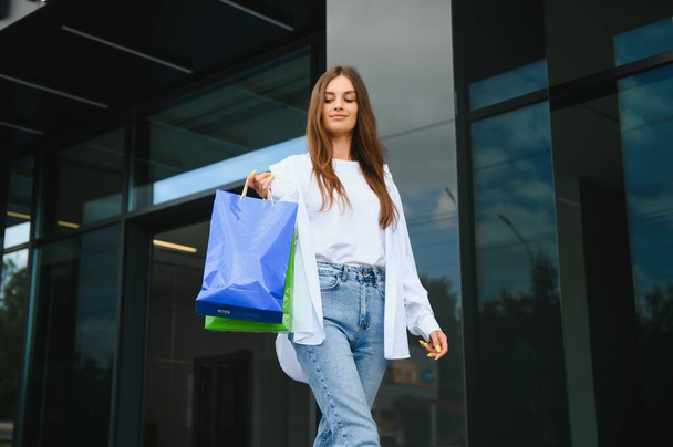 Beautiful young woman with shopping bags near shop outdoors - Foto, Imagem