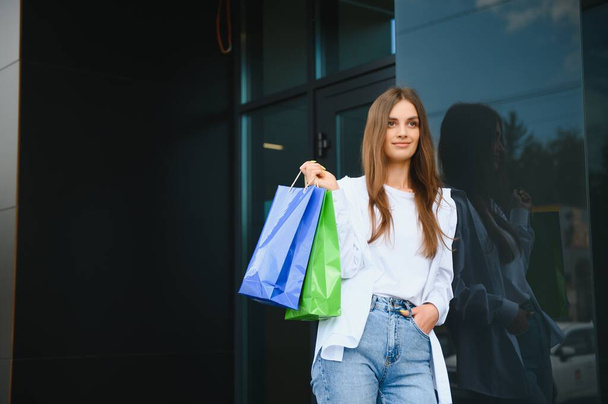 Beautiful young woman with shopping bags near shop outdoors - Photo, image