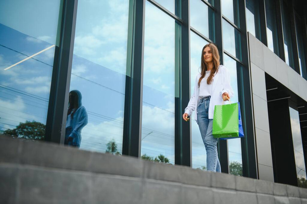 Beautiful young woman with shopping bags near shop outdoors - Φωτογραφία, εικόνα