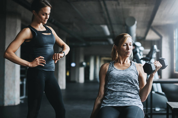 Du bist stärker, als du denkst, schieb es. eine reife Frau stemmt Gewichte mit einer Trainerin im Fitnessstudio - Foto, Bild