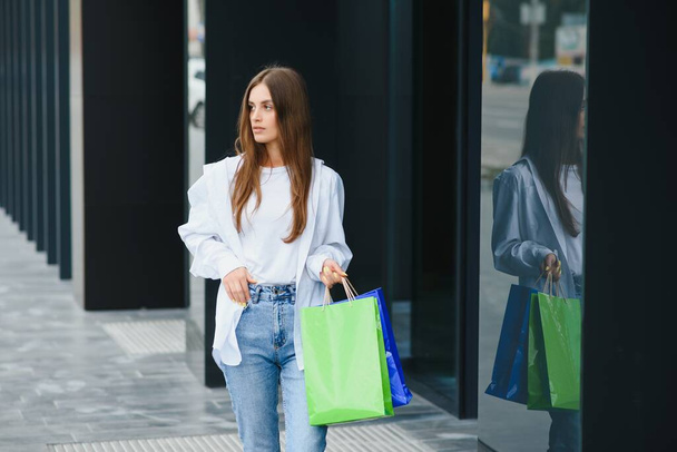 Beautiful young woman with shopping bags near shop outdoors - Fotoğraf, Görsel