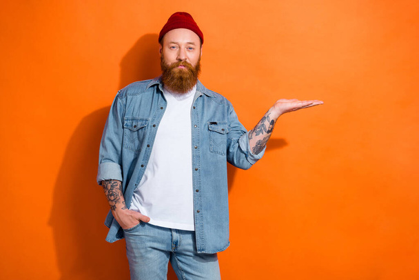 Photo of hipster young man beard red hair wear denim style outfit hold hand new sales system product mockup isolated on orange color background. - Photo, image
