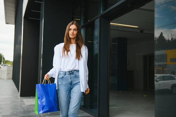 Beautiful young woman with shopping bags near shop outdoors - Foto, Imagen
