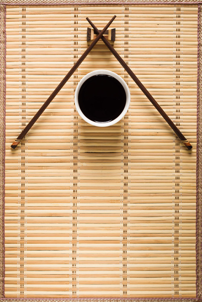 Chopsticks and bowl with soy sauce on bamboo mat - Fotó, kép