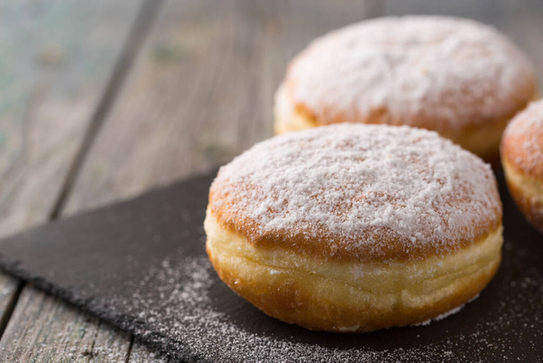 Ruddy delicious donuts berliners with filling sprinkled with powdered sugar on a rustic background - Photo, Image