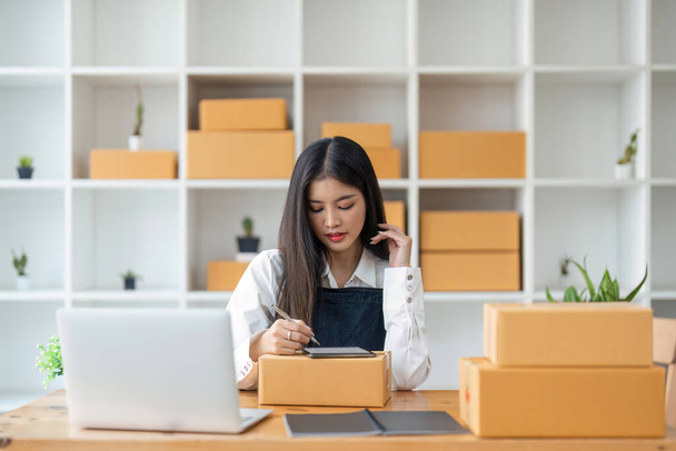 Uruchomienie małych przedsiębiorstw MŚP przedsiębiorca niezależny azjatycki kobieta za pomocą tabletu i pudełka, aby otrzymywać i przeglądać zamówienia online, aby przygotować się do pakowania sprzedaży klientom, online sme pomysłów biznesowych. - Zdjęcie, obraz