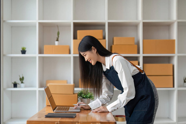 Стартап SME невеликий бізнес-підприємець вільної азіатської жінки за допомогою ноутбука і коробки, щоб отримати і переглянути замовлення онлайн, щоб підготуватися упаковка продажу клієнтам, онлайн sme бізнес ідеї. - Фото, зображення
