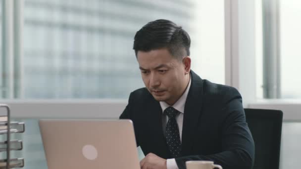 uomo d'affari asiatico di successo che lavora in ufficio guardando computer portatile - Filmati, video