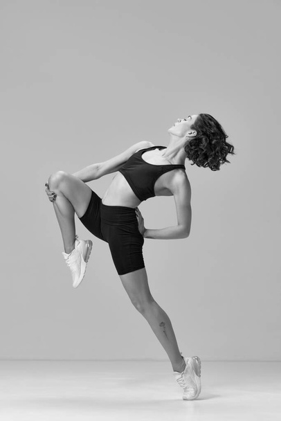 Black and white image. Young sportive woman in sportswear training, doing stretching exercises. Graceful movements. Concept of sportive lifestyle, beauty, body care, fitness, health - Foto, Imagen