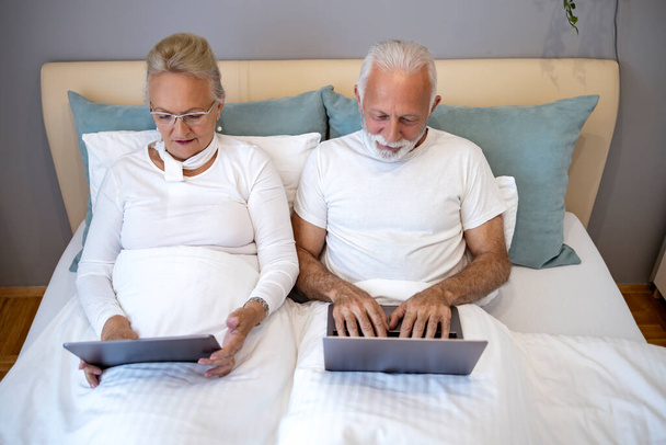 Gelukkig senior paar met behulp van laptop tijdens het liggen in de slaapkamer.Technologie en ouderen concept. - Foto, afbeelding