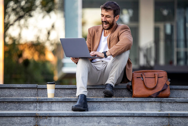 Giovane uomo di successo che lavora su laptop outdoors.Young uomo seduto sulle scale e utilizzando il computer portatile. - Foto, immagini