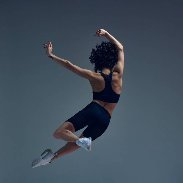 High jump. Relief back, Dynamic image of young beautiful woman in sportswear training, posing in motion against grey studio background. Sportive lifestyle, beauty, body care, fitness, health concept - Φωτογραφία, εικόνα