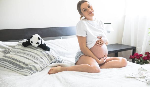 Mulher grávida sentada em uma cama segurando.O conceito de gravidez, maternidade e pré-natal. Mãe com uma nova vida. - Foto, Imagem