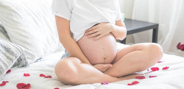Terhes nő ül egy ágyban gazdaság. A koncepció a terhesség, az anyaság és a terhesgondozás. Anya egy új élettel. - Fotó, kép
