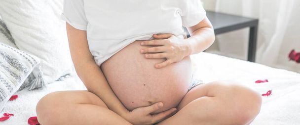 Těhotná žena sedí na posteli drží. Koncept těhotenství, mateřství a prenatální péče. Máma s novým životem. - Fotografie, Obrázek