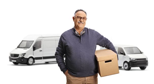 Mature man with a cardboard box standing in front of vans isolated on white background  - Fotó, kép